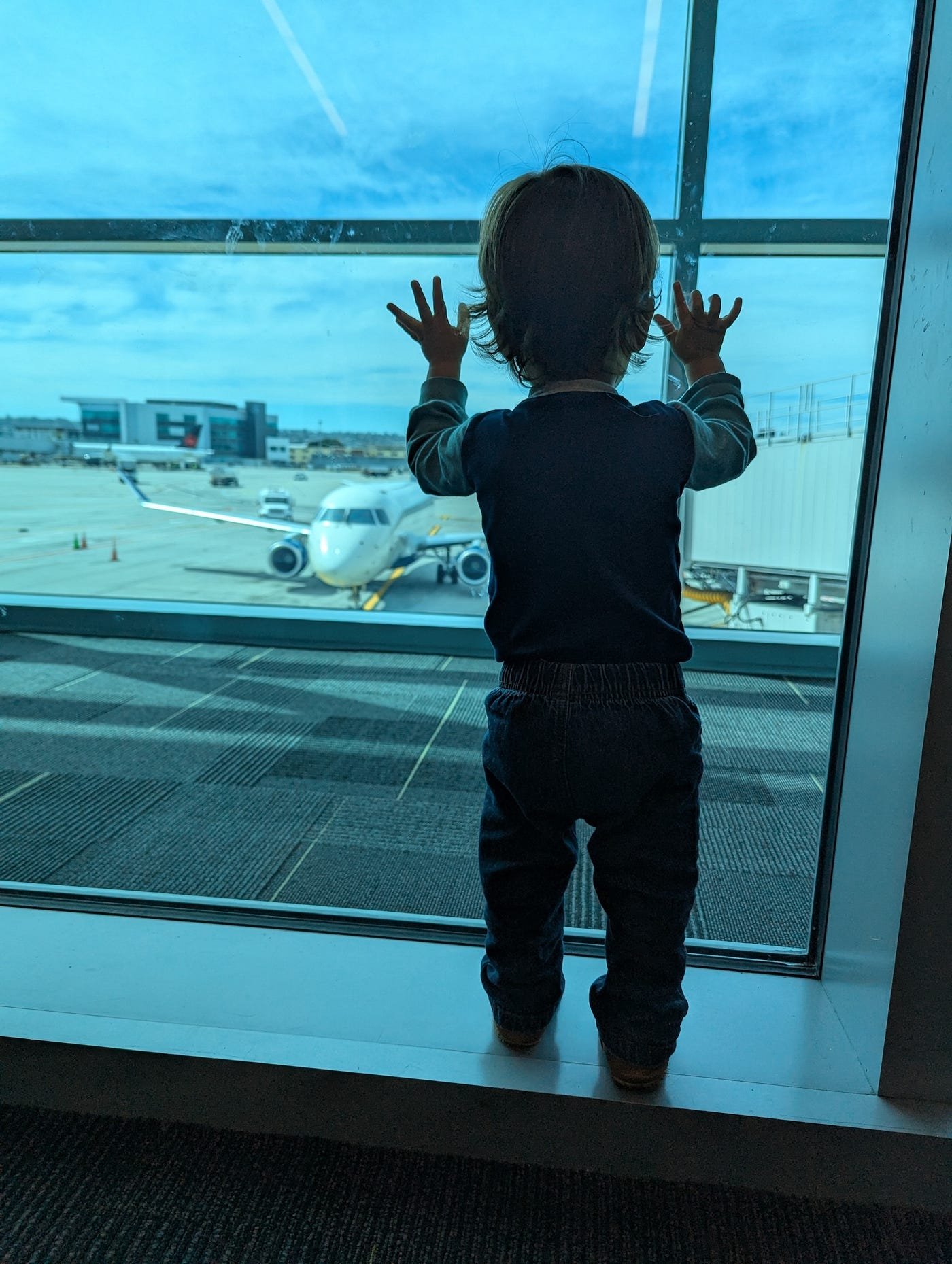 Baby looking out the airport window at a plane at its gate