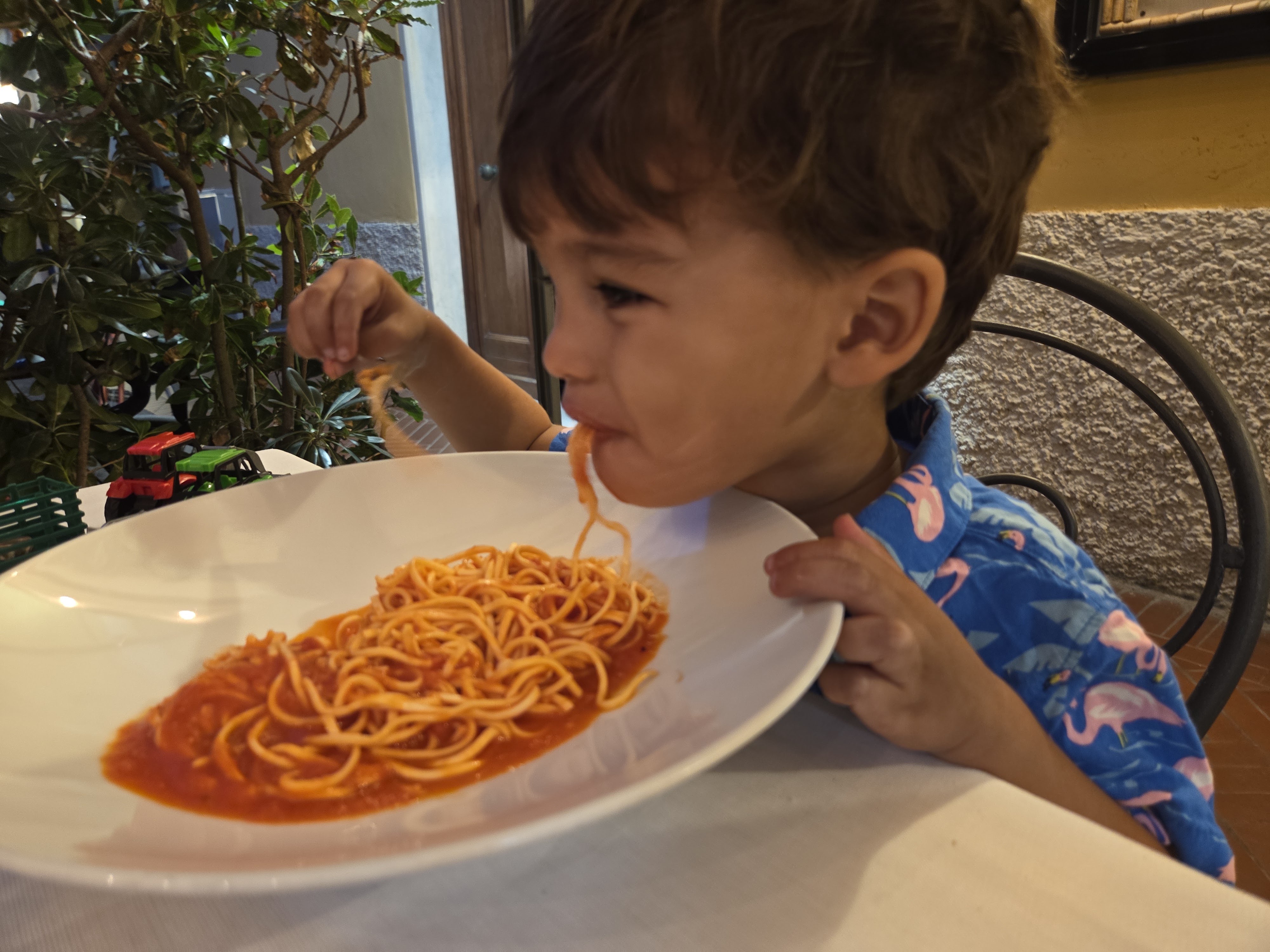Arlo eating a plate of spaghetti with tomato sauce at an outdoor restaurant table