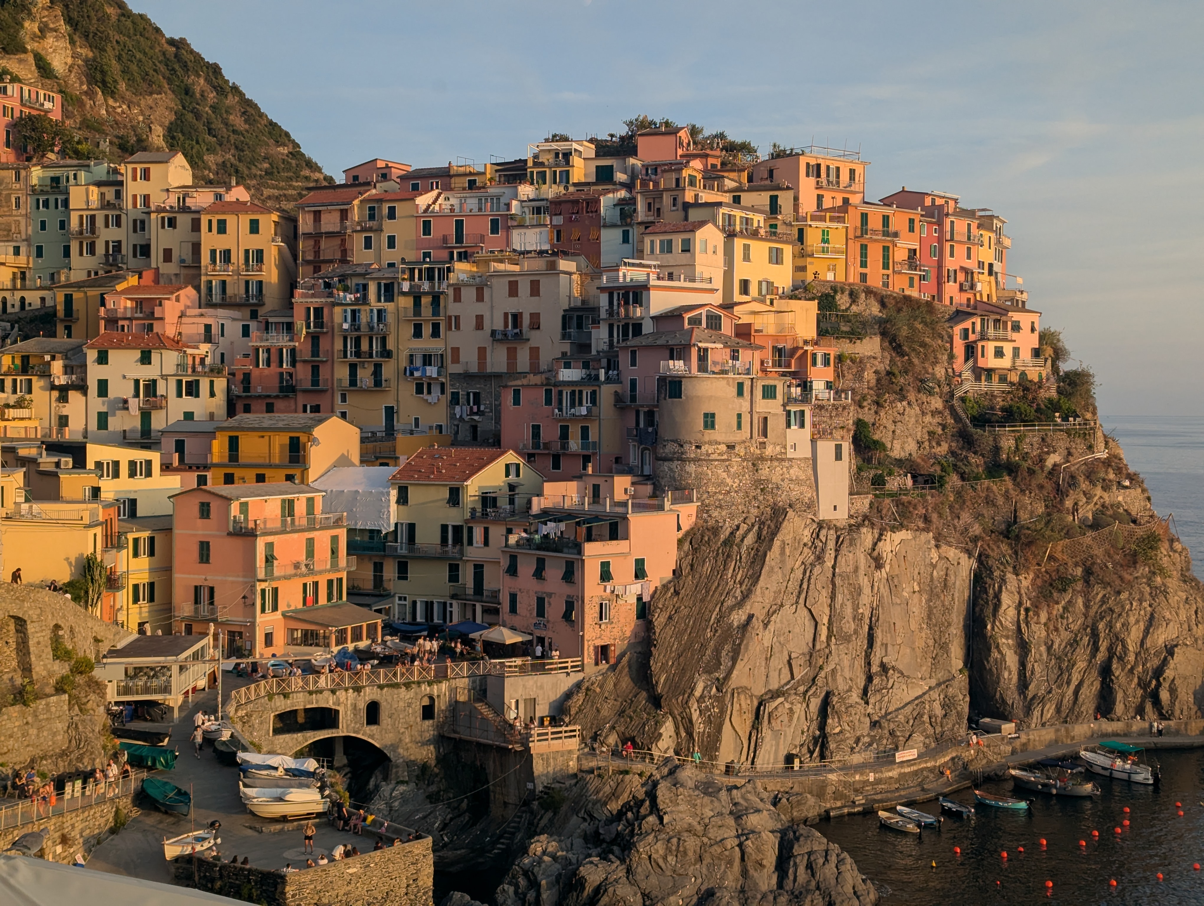 Manarola's stacked colorful buildings on a cliff over the harbor, lit gold in the late afternoon sun