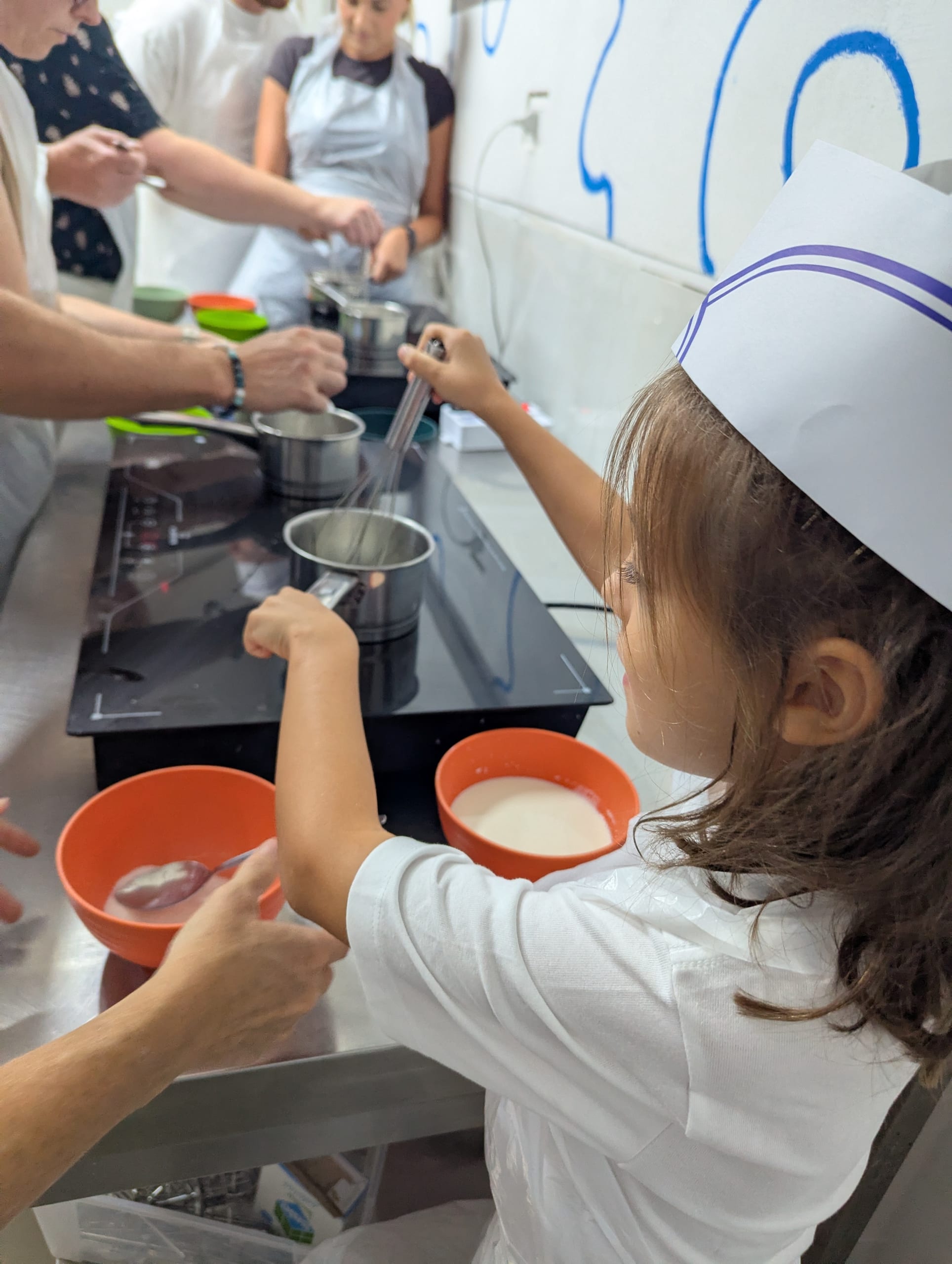Remi in a paper chef hat whisking the gelato base in an orange bowl at the cooking class