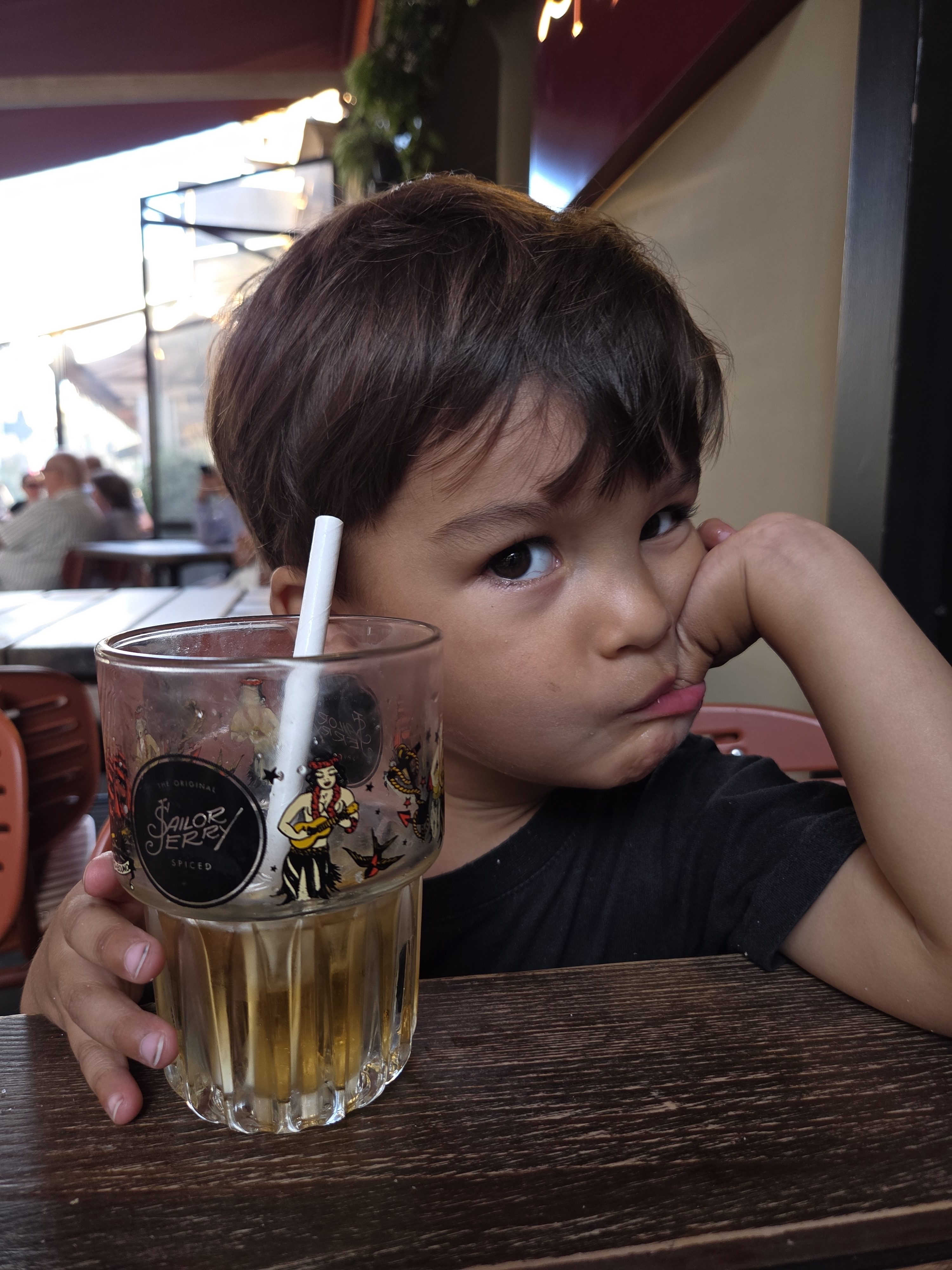 Close-up of Arlo resting his chin on his hand at a restaurant table, holding a glass with a straw and looking tired after a long day