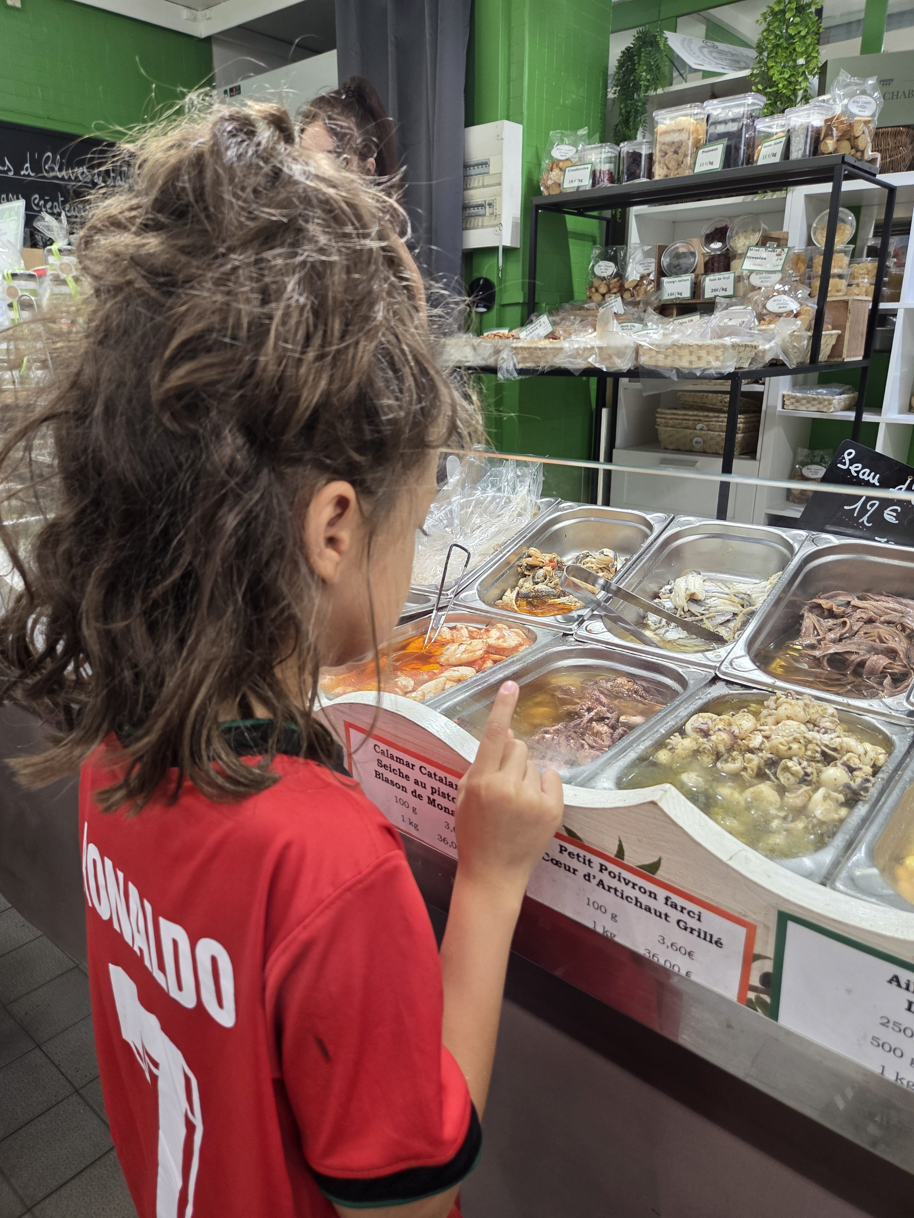 Remi from behind pointing at trays of marinated squid, octopus, and seafood at a Les Halles prepared-food counter