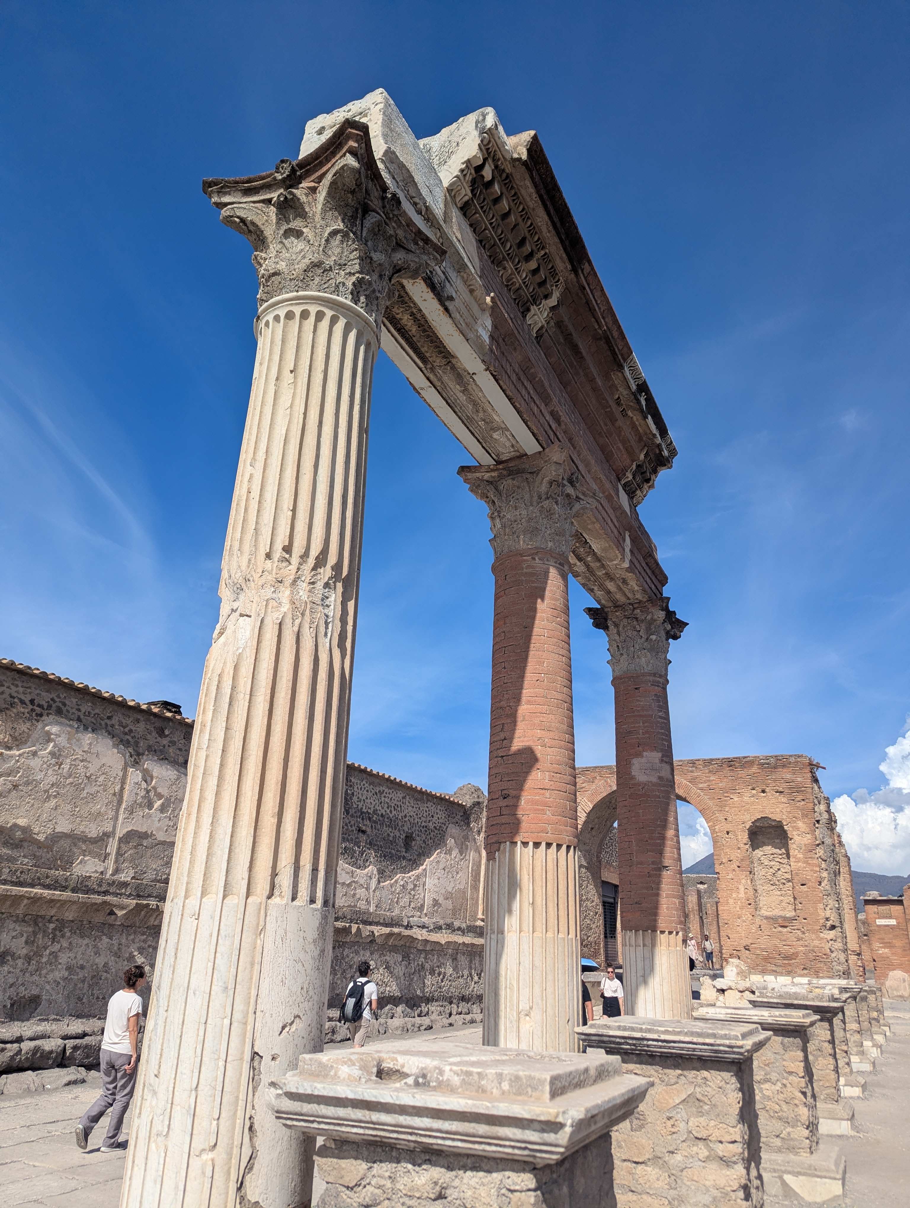 A fluted marble column in the foreground with the reconstructed columns of the Temple of Venus behind it, under a bright blue sky