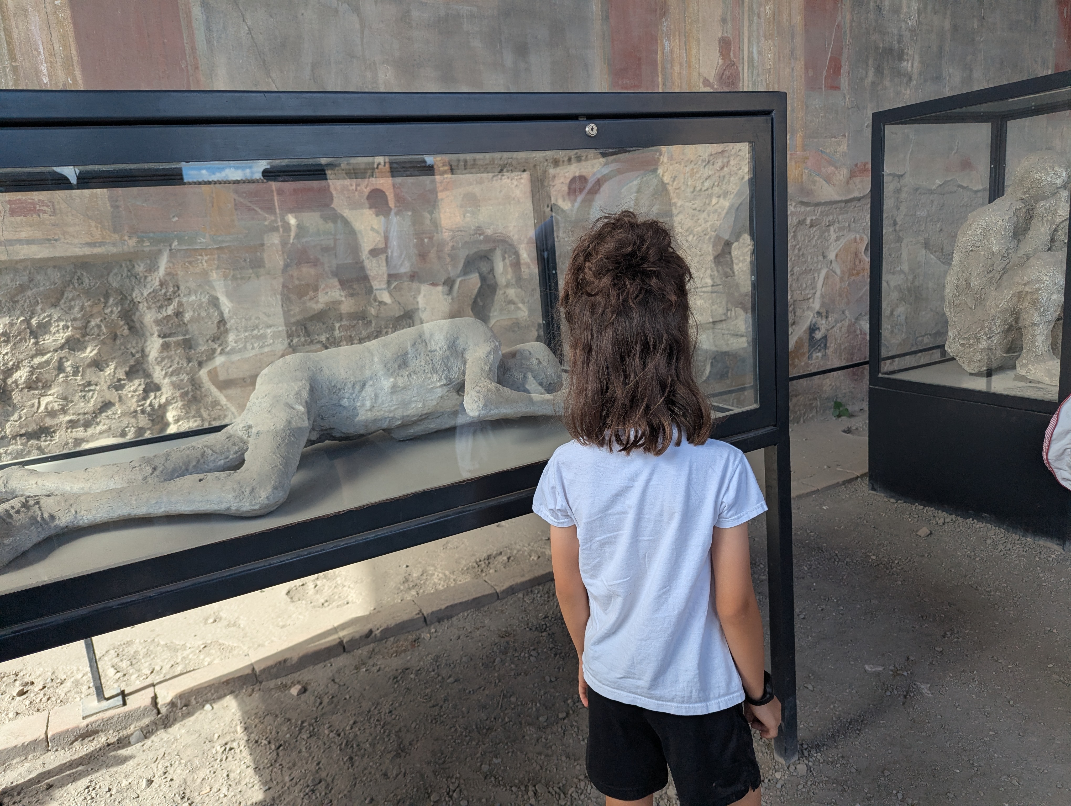 Remi looking into a glass case at a plaster cast of a Pompeii victim, frescoed walls visible behind
