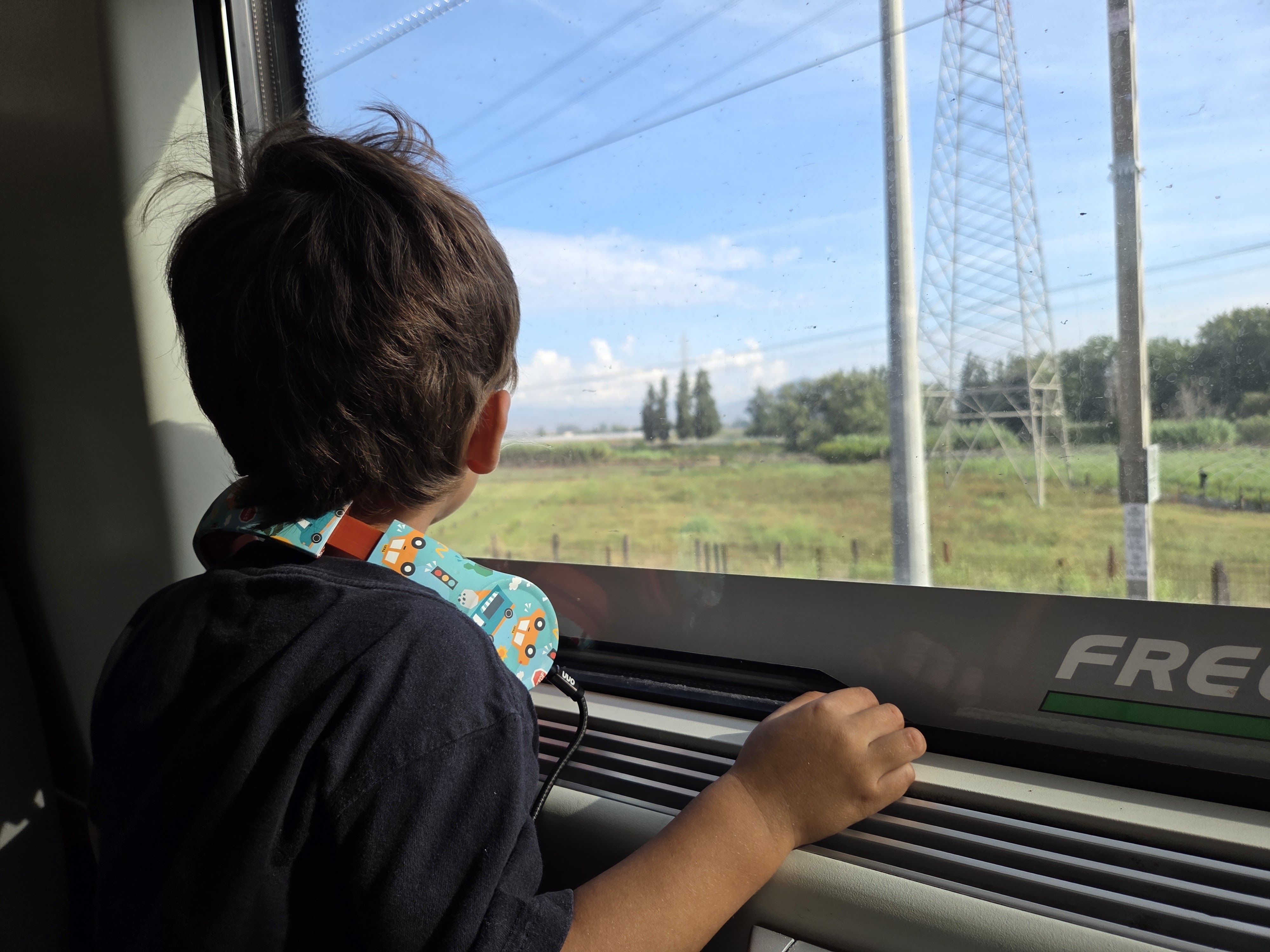 Arlo looking out a train window at the Italian countryside, an electrical pylon and green fields passing by