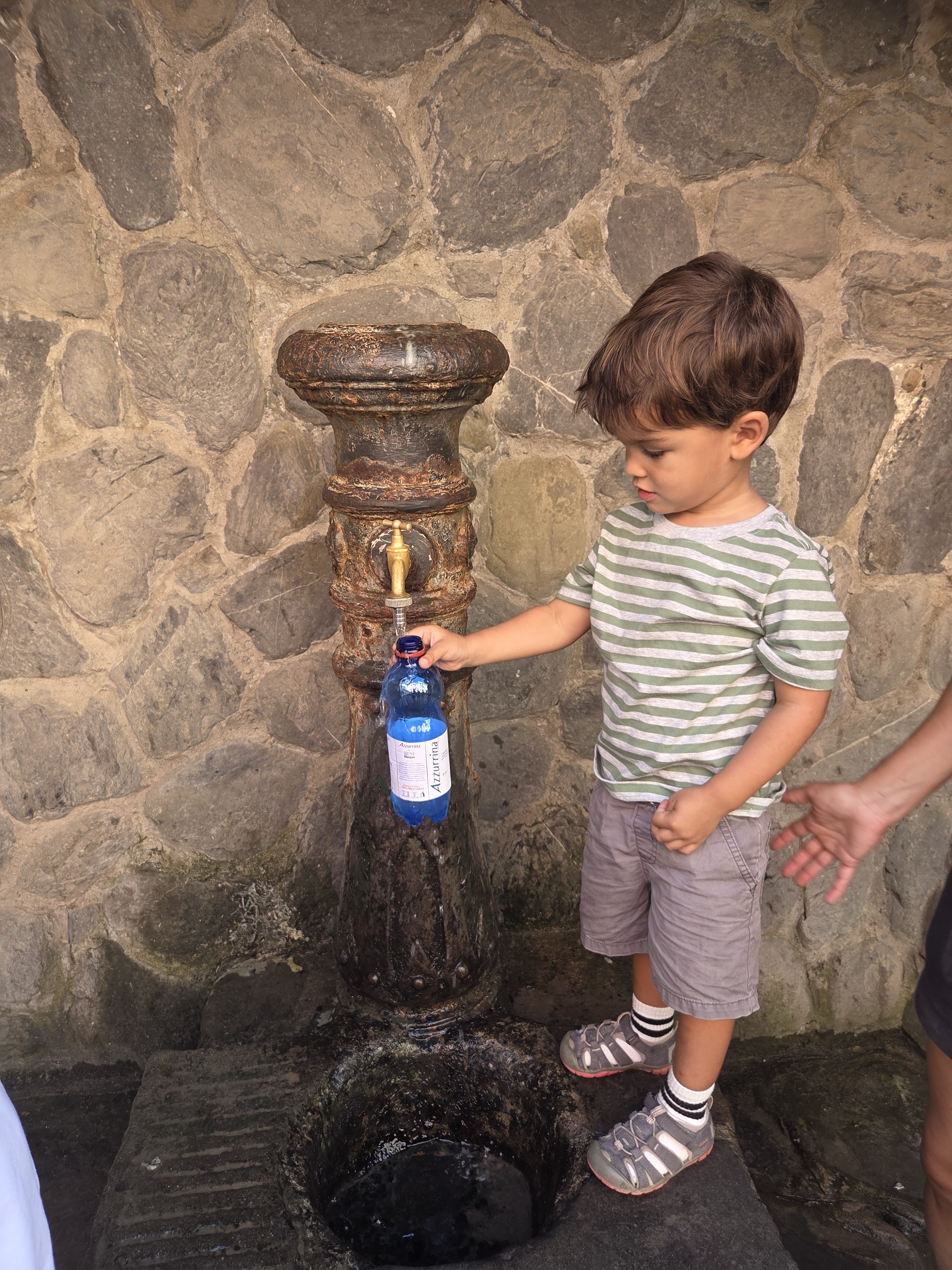 Arlo filling a water bottle from an old stone fountain built into a wall in Vernazza