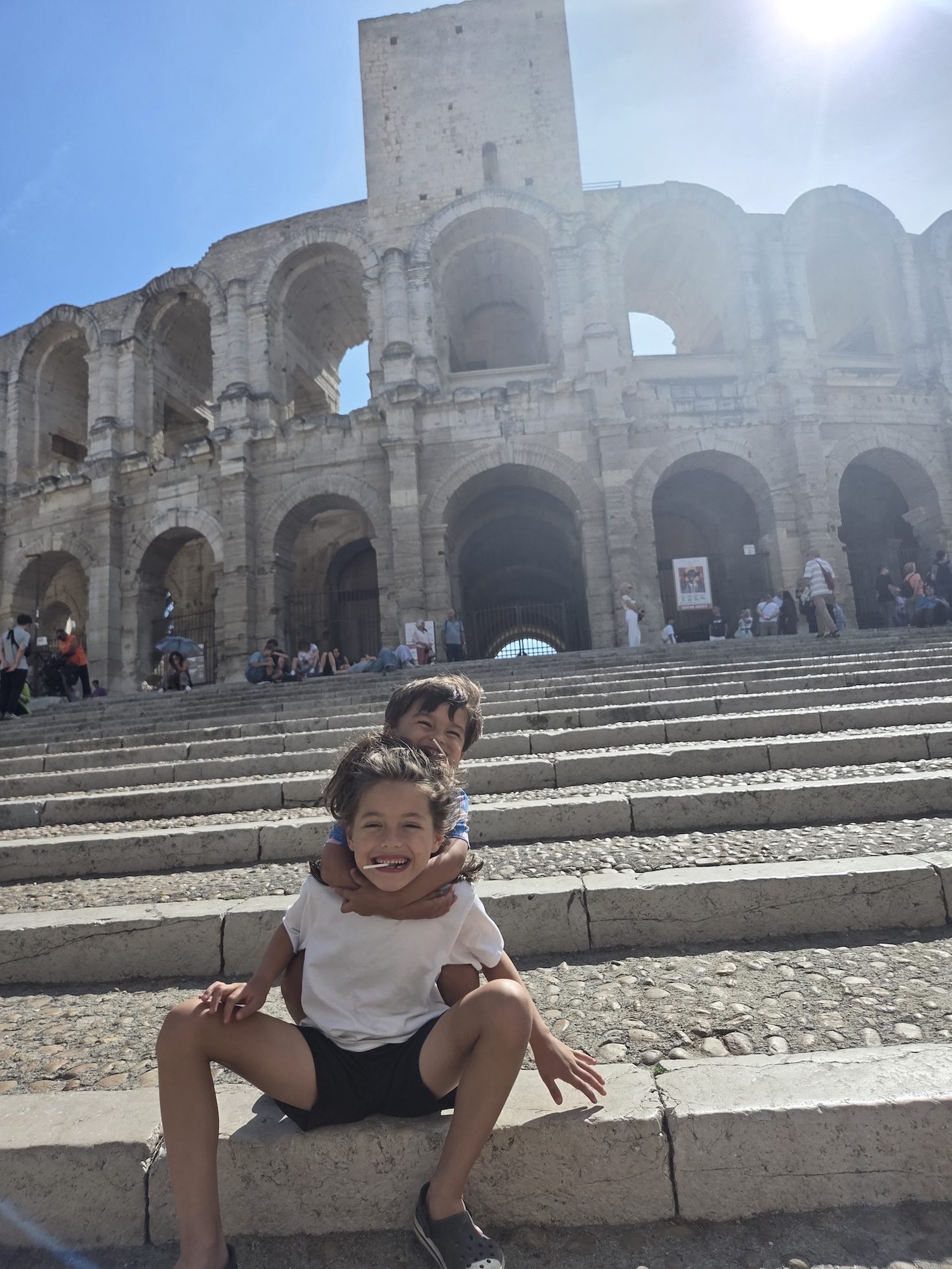 Remi sitting on the stone steps in front of the arena with Arlo on her back, both beaming