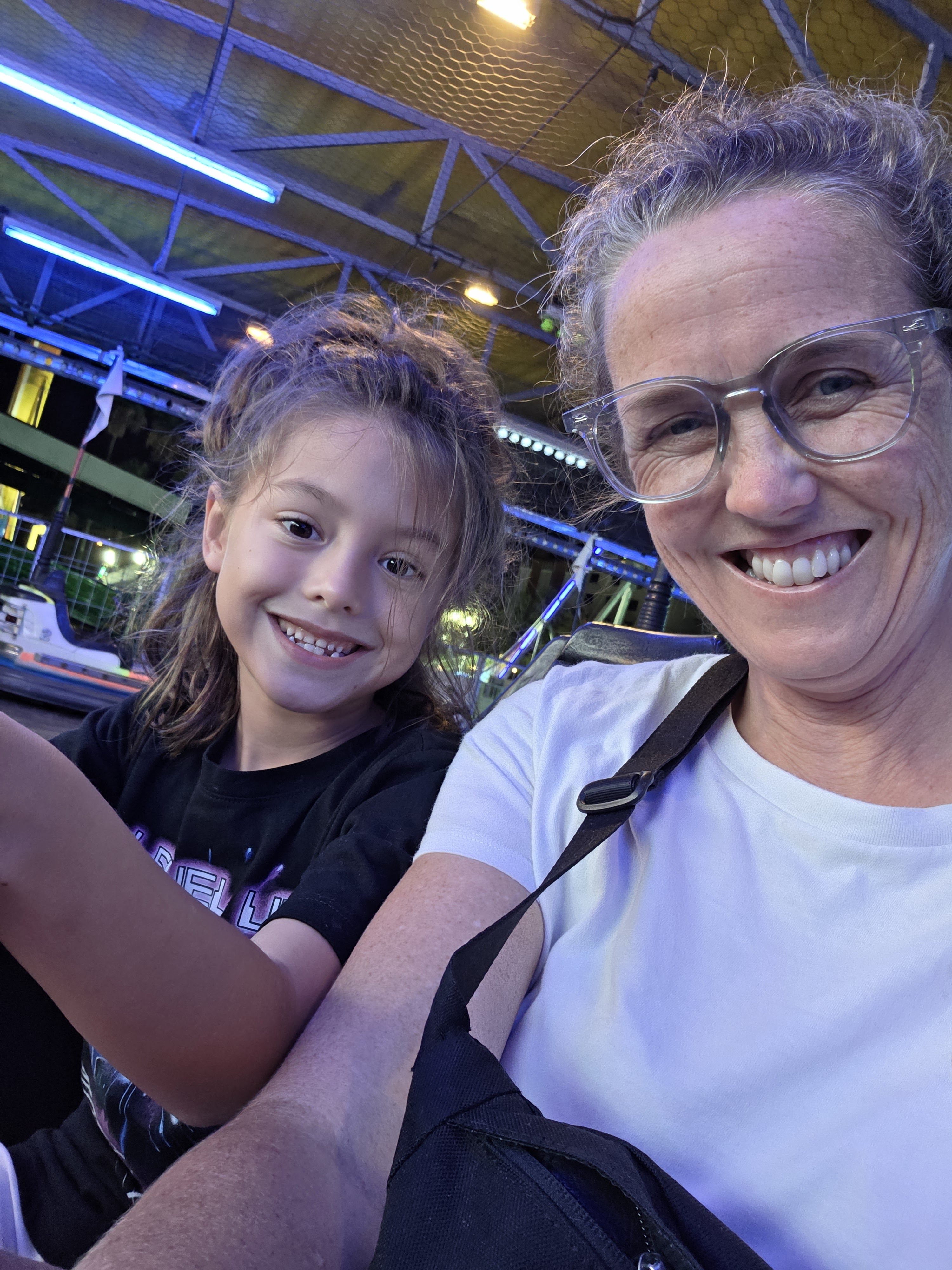 Remi and Dani grinning in a selfie at a bumper car ride lit with blue lights