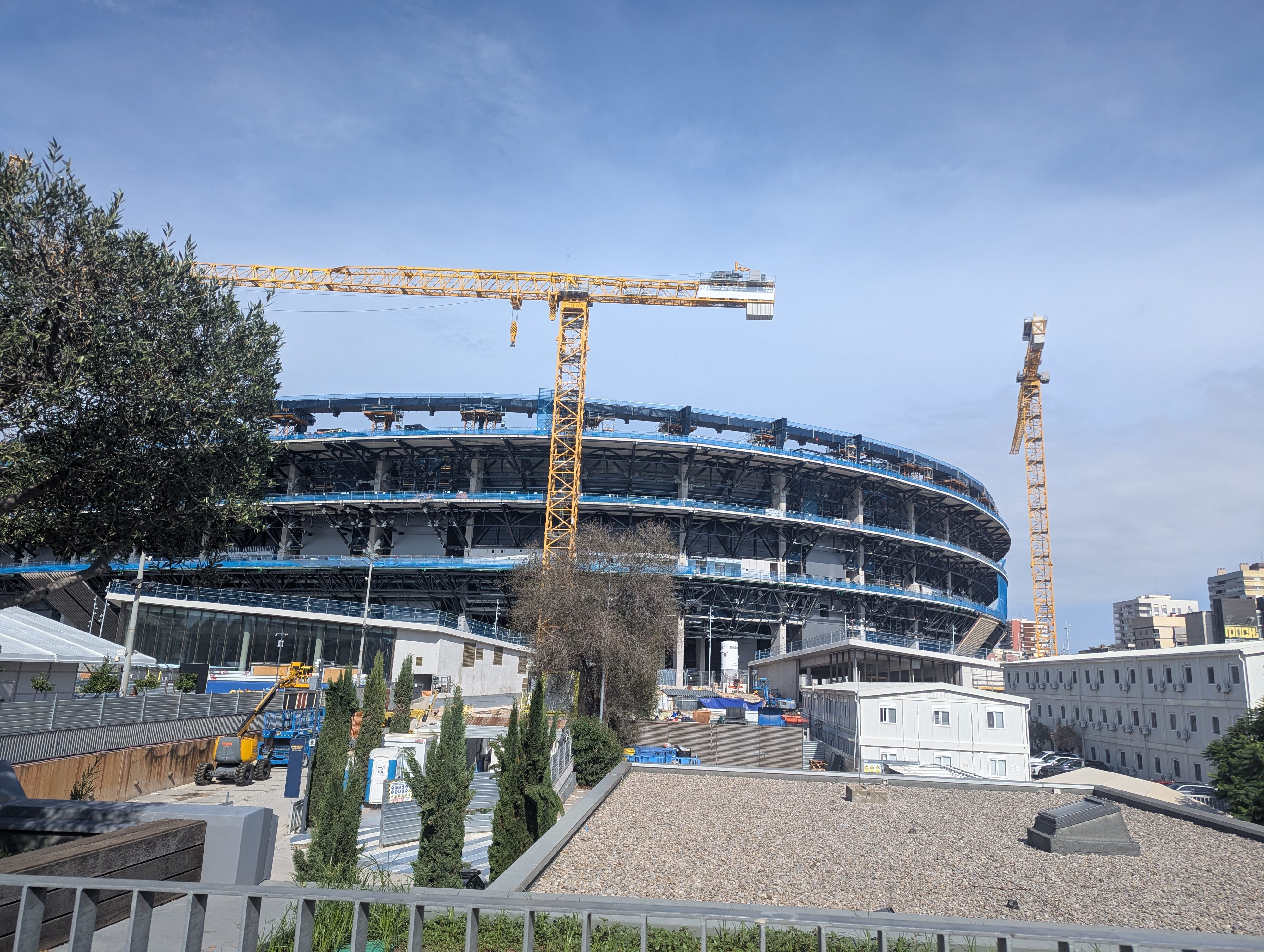 The Camp Nou stadium partly under renovation, with construction cranes beside its curved upper ring on a sunny day
