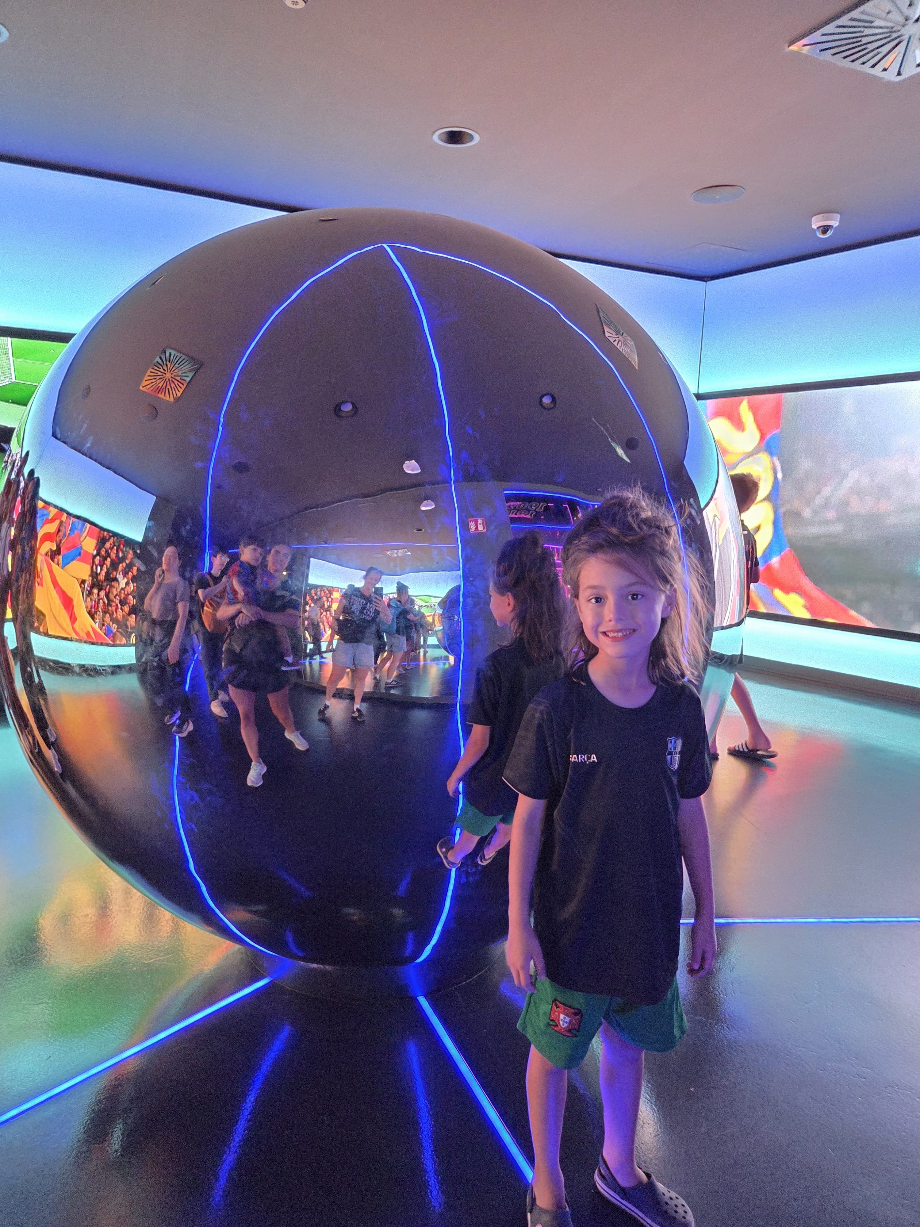 Remi standing beside a large mirrored sphere in a glowing blue museum room