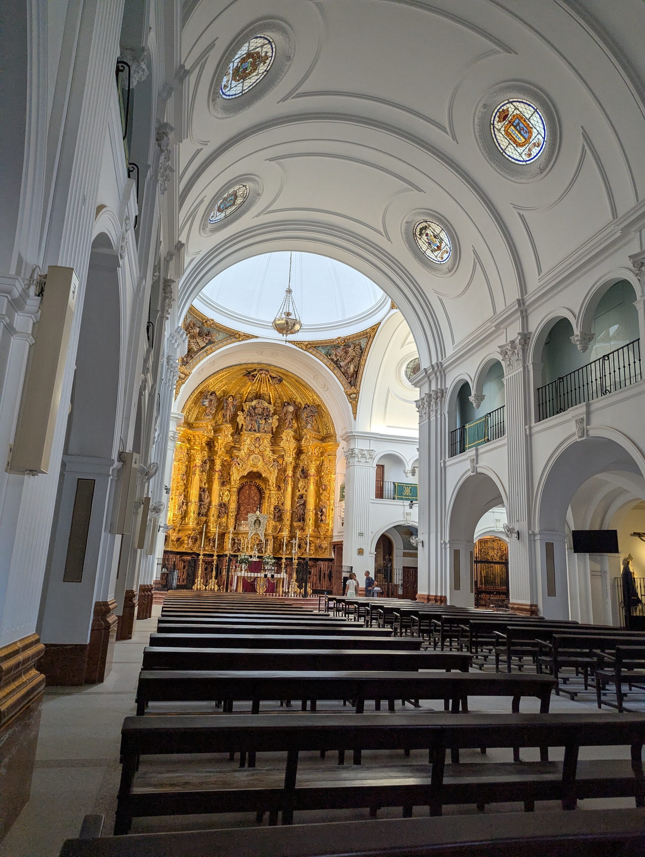 Inside the church in El Rocío, rows of dark wooden pews leading to a gilded golden altar under a white domed ceiling