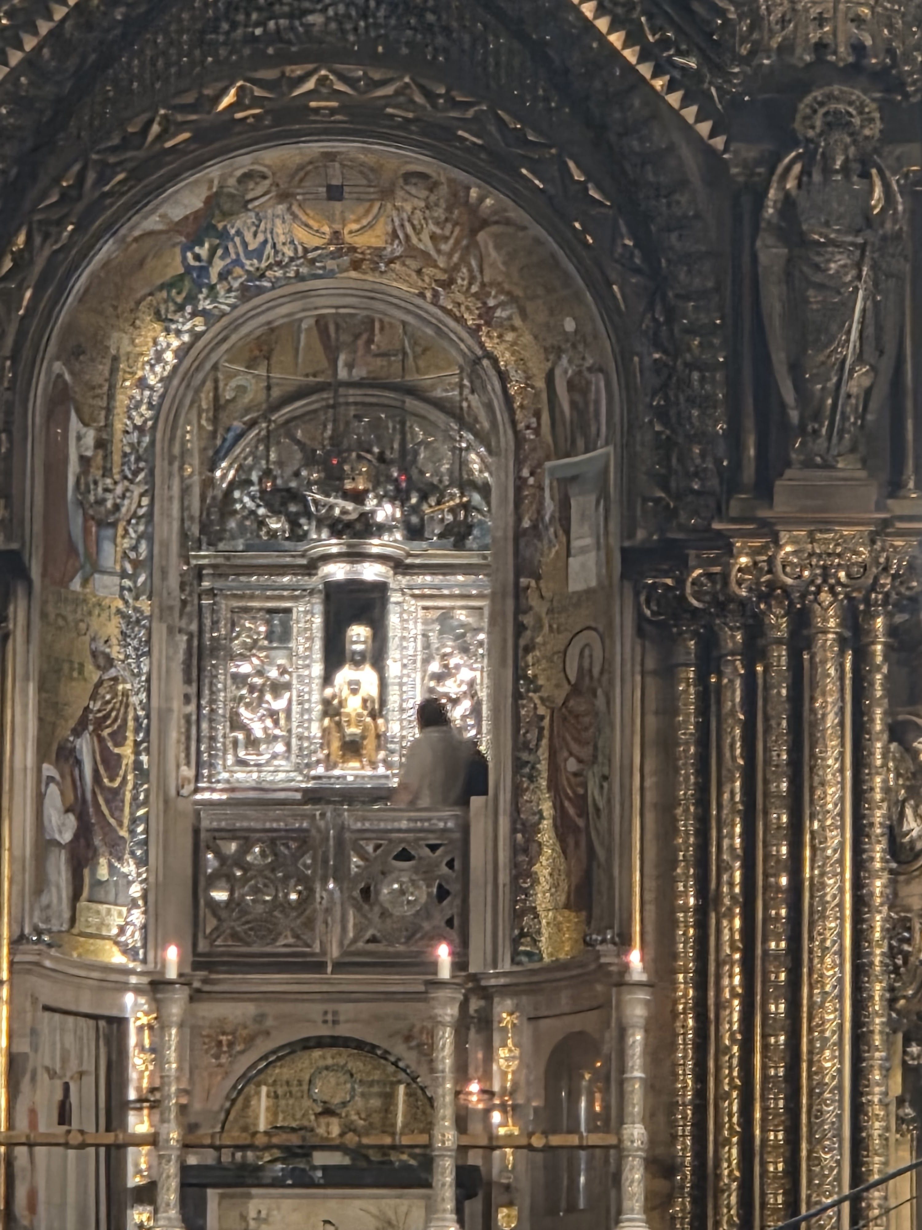 The ornate gold altar of the Montserrat basilica with the small dark statue of the Black Madonna in a niche above it, candles lit below