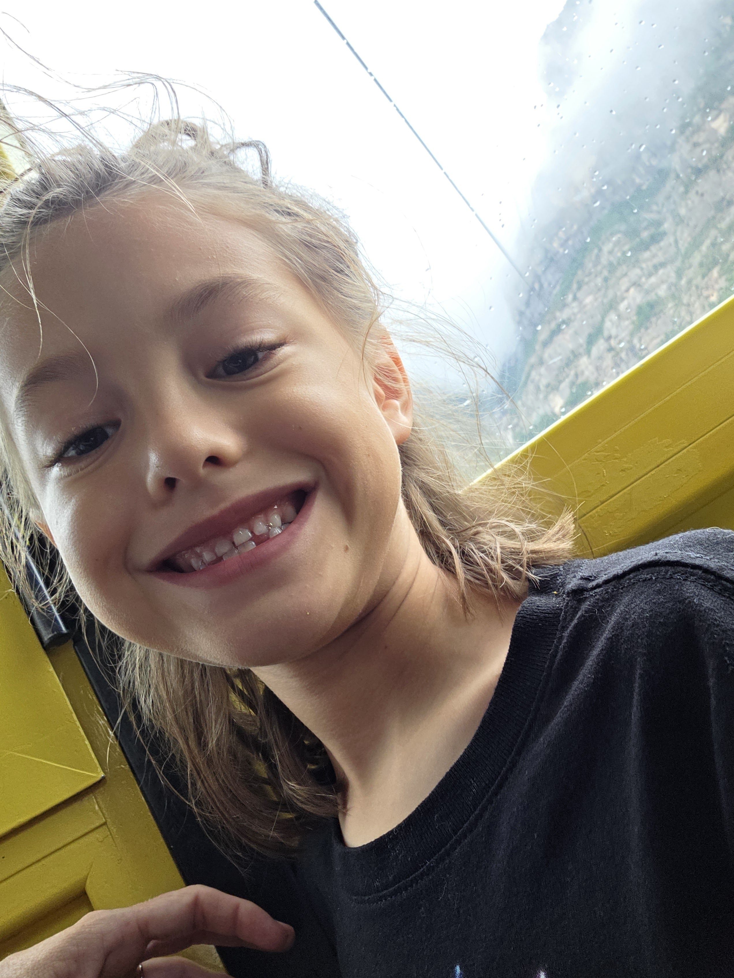 Remi grinning in a selfie inside the yellow cable car, wind in her hair and the misty mountains through the window behind her