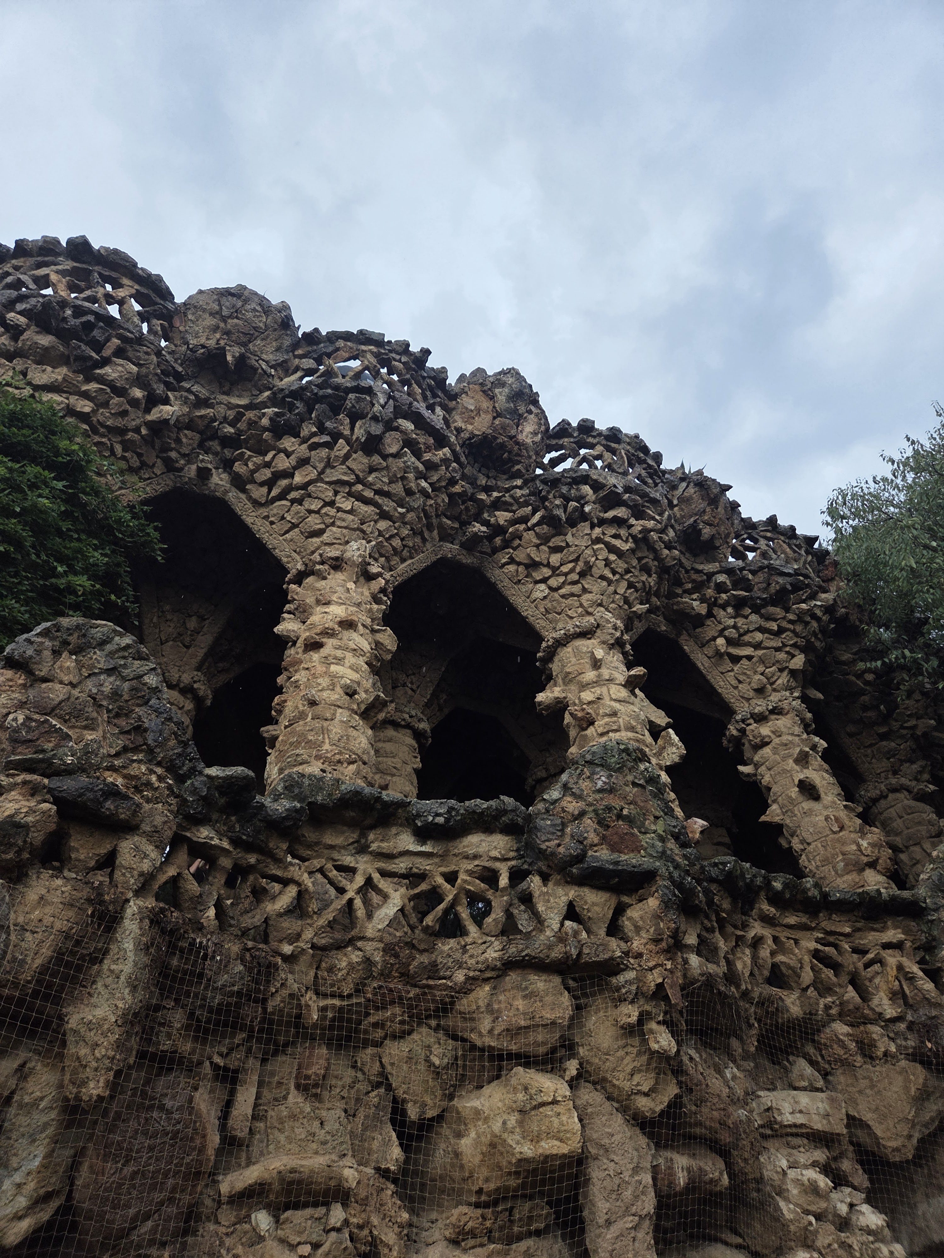 Rough stone arches and columns in Parc Güell under a cloudy sky