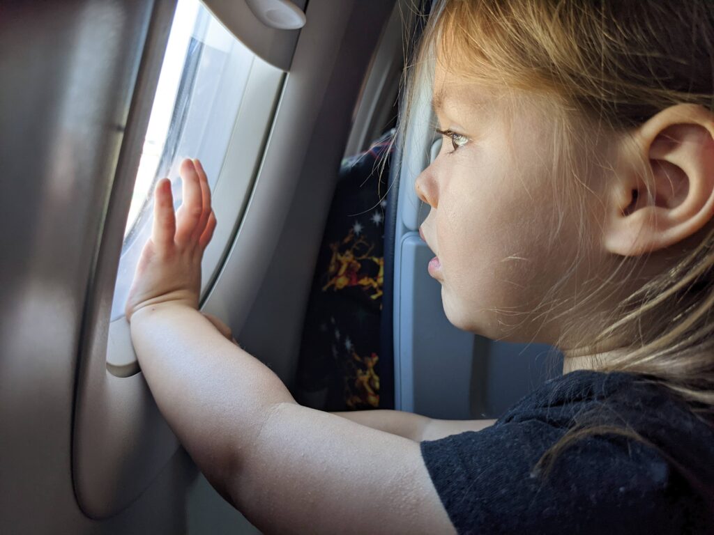 Toddler looking out of airplane window - what to pack when traveling with kids